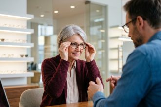 Femme d'une cinquantaine d'années essayant des lunettes chez un opticien professionnel dans une optique moderne
